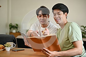 A smart Asian male college student is tutoring to his friend while studying at home together