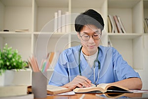 Smart young Asian male medical student reading a book, preparing for exam
