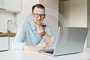 Smart young man sits at the kitchen desk and works remotely from home