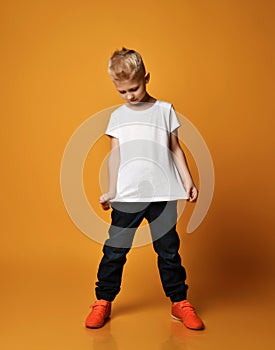 Smart young schoolboy kid in blue jeans and sneakers stands looking at his white blank t-shirt