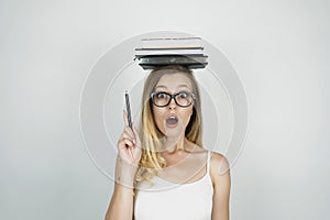 Smart young woman in glasses holding pen in her hand and books on her head isolated white background