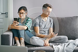 Smartphone addicted couple scrolling through social networks using phones sitting on the couch at home