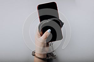 Smartphone addiction concept. Phone chained to handcuff in hand on a grey background