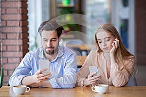 Smartphone addiction and phubbing concept. Young couple on boring date, stuck in gadgets, neglecting each other at cafe photo