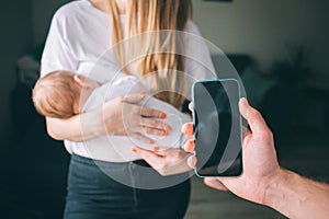 Smartphone application for a young family . Mother holds a newborn baby in her arms. And Father shows the phone screen