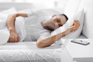 Smartphone on bedside table near sleeping man