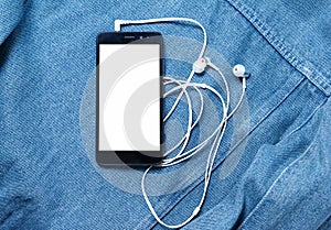 Smartphone with black case and a blank white screen and plugged in headphones ear buds on the background of denim