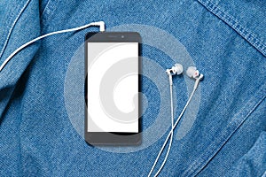Smartphone with black case and a blank white screen and plugged in headphones ear buds on the background of denim