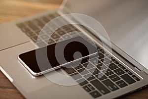 Smartphone with black screen placed on laptop computer keyboard, closeup. Modern technologies in everyday life