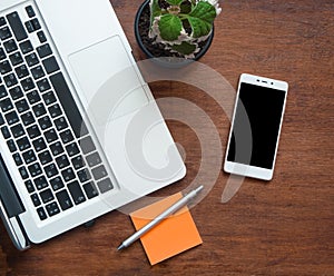 Smartphone with blank black screen and part of laptop keyboard on wooden desk