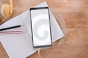 Smartphone with blank screen on blank notebook on wood table