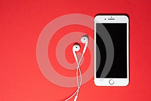 Smartphone with Blank Screen Connects to Earphones with Spiral Cable on Red Background Top View