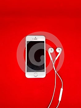 Smartphone with Blank Screen Connects to Earphones with Spiral Cable on Red Background Top View