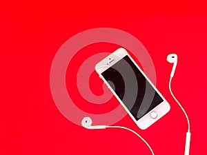 Smartphone with Blank Screen Connects to Earphones with Spiral Cable on Red Background Top View