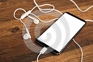 Smartphone with blank screen and headphones on a wooden table. Top view. Mockup