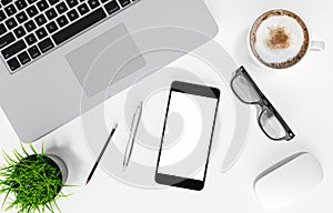 Smartphone with blank screen, laptop, coffee cup, glasses, pen and pencil on white office desk table, top view, workspace design,