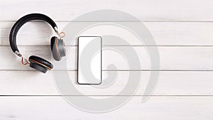 Smartphone with blank screen and wireless headphones on wooden background