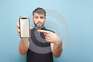 Smartphone with a blank white screen in the hands of an adult man with a beard, wearing a dark shirt and standing on a blue