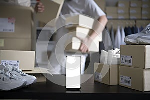 Smartphone with blank white screen standing on the desktop in the warehouses. Asian man online seller checking stock photo