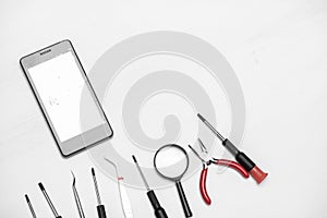 Smartphone with broken and cracked screen with tools for repair on white background