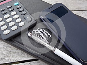 Business concept with agenda, mobile phone, calculator, stylus pen and paperclips.