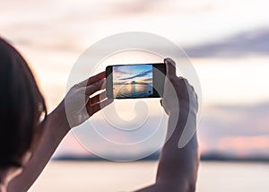 Smartphone camera in tourist woman personâ€™s hands who taking photo on touch screen of beautiful seascape sky with clouds