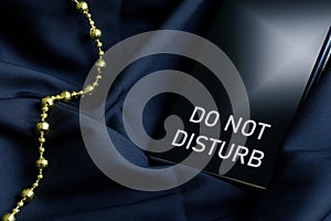 Smartphone cell phone with the inscription do not disturb next to decorative gold thread on a dark silk fabric. The concept of