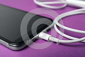 Smartphone and charge cable on purple background. Modern technology