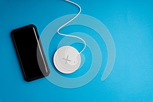 Smartphone charging on a charging pad or dock on blue background