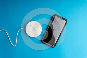 Smartphone charging on a charging pad or dock on blue background.Wireless charging