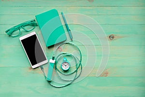 Smartphone charging by power bank, alarm clock, paper notebook, pen and eyeglasses on wooden background