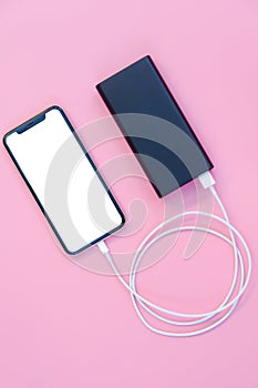 Smartphone charging with power bank on pink background. white screen or blank screen with clipping path for copy space. Flat lay