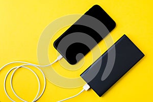Smartphone charging with power Bank via USB cable on yellow background top view