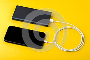 Smartphone charging with power Bank via USB cable on yellow background top view