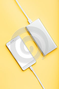 Smartphone charging with power bank by wire on yellow background