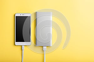 Smartphone charging with power bank by wire on yellow background