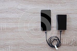 Smartphone charging with power bank on wood background