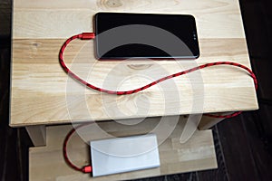 Smartphone charging with power bank on wooden chair