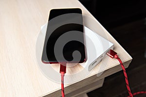 Smartphone charging with power bank on wooden table