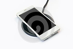 Smartphone charging on a wireless charger on white background. black screen or blank screen with clipping path for copy space.