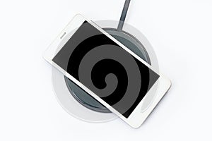 Smartphone charging on a wireless charger on white background. black screen or blank screen with clipping path for copy space.