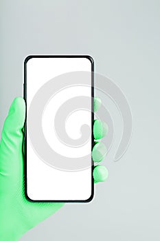 A smartphone with a clean white screen in the hand in a green medical glove close-up.