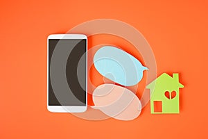Smartphone with clipping path on touchscreen,  house paper cut and couple bubble speech paper on orange background and copy space