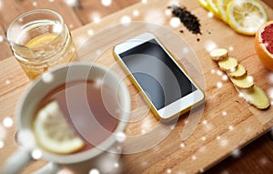 Smartphone with cup of lemon tea, honey and ginger