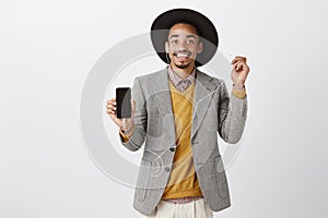 Smartphone definitely worth buying. Portrait of satisfied good-looking african customer in classy suit and hat, showing