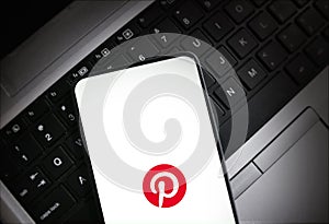 Smartphone displaying Pinterest logo on laptop keyboard illustrative editorial technology and social media