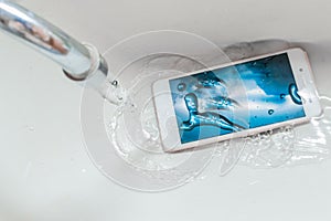 Smartphone dropped into the sink under the water. Concept mobile phone repair. Recessed phone into the water photo