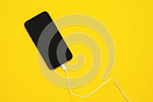 Smartphone is facing up, usb lightning cable or wired headphones are connected to mobile phone connector on yellow background, top