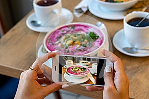 Smartphone food photography carrot soup in bowl. Woman hands take phone photo of dinner or lunch for social networks.