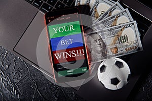 Smartphone with gambling mobile application, ball and money banknotes on a keyboard close-up. Sport and betting concept